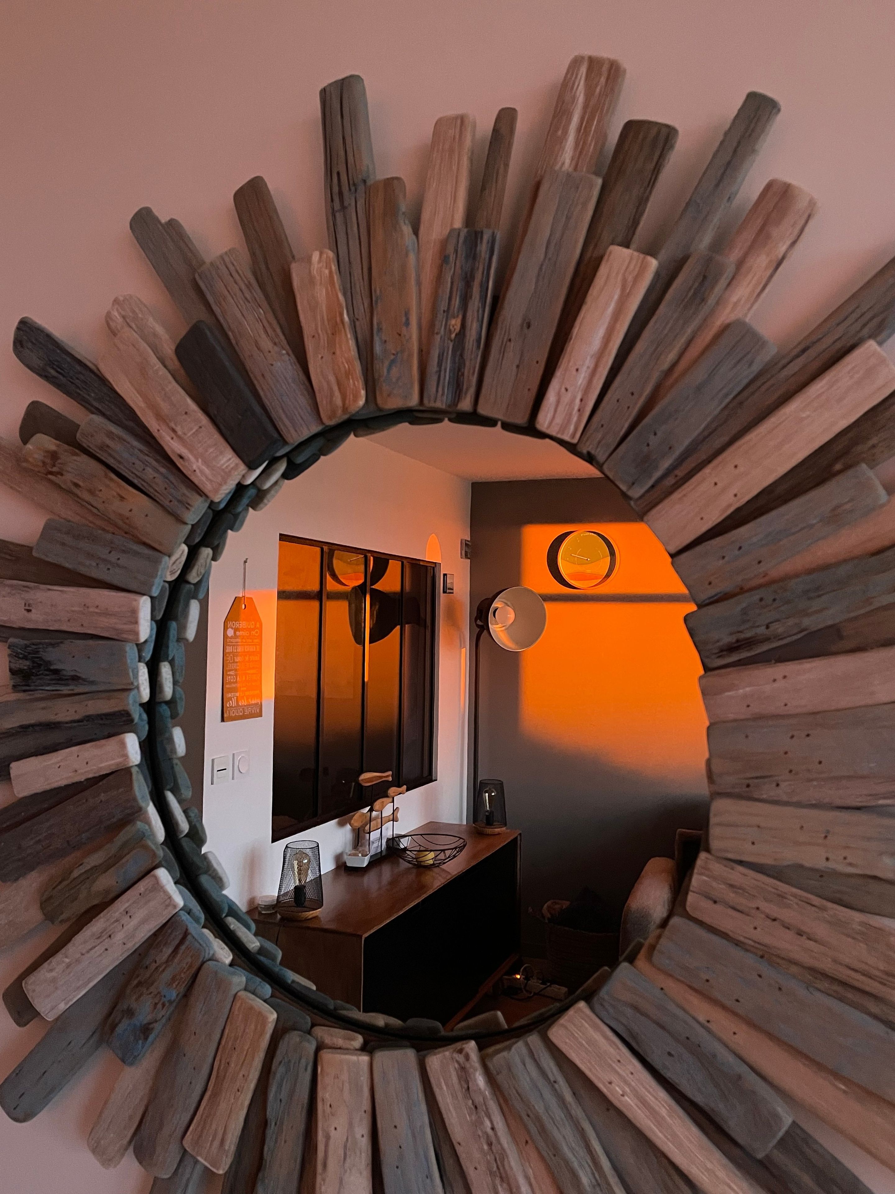 Un miroir avec un cadre en bois, qui reflète une pièce comprenant un bureau, une chaise et une horloge fixée au mur.