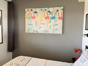 Un dormitorio con cama, un cuadro colgado en la pared, una ventana con cortinas y una lámpara de noche.