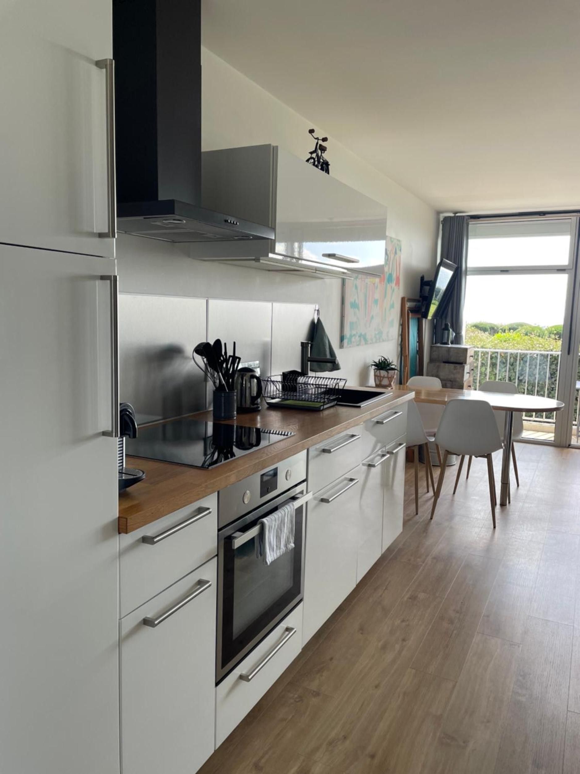 Une cuisine moderne avec des meubles blancs, un plan de travail en bois et un coin repas comprenant une table et des chaises.