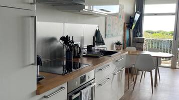 Une cuisine moderne avec des meubles blancs, un plan de travail en bois et un coin repas comprenant une table et des chaises.