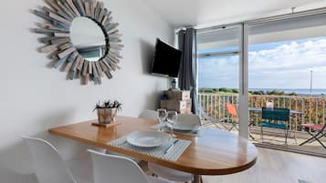 Een eetgedeelte met een houten tafel, witte stoelen, een decoratieve spiegel en een flatscreen televisie.