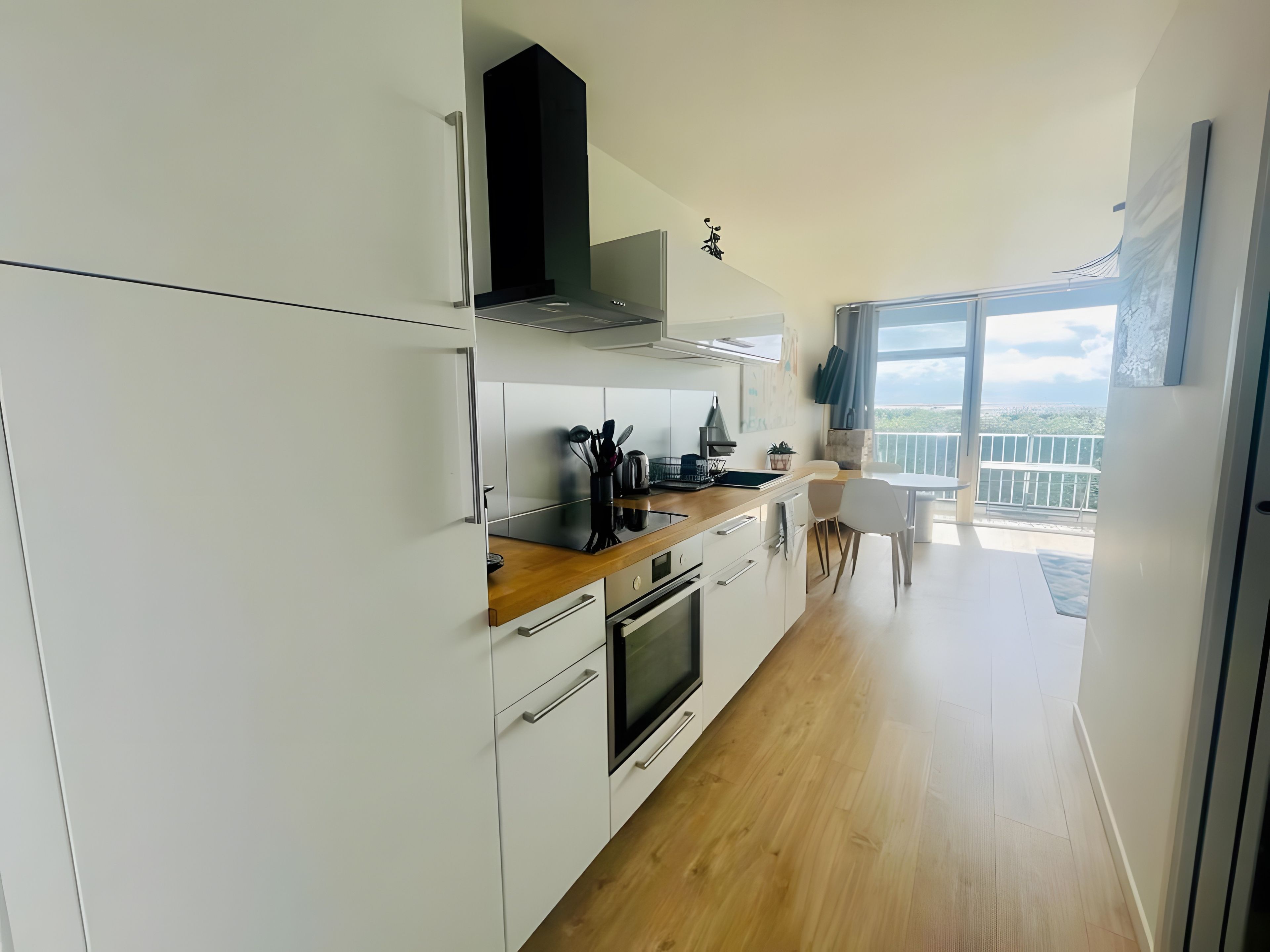 Een moderne keuken met witte kastjes, een houten aanrecht en uitzicht op het balkon.
