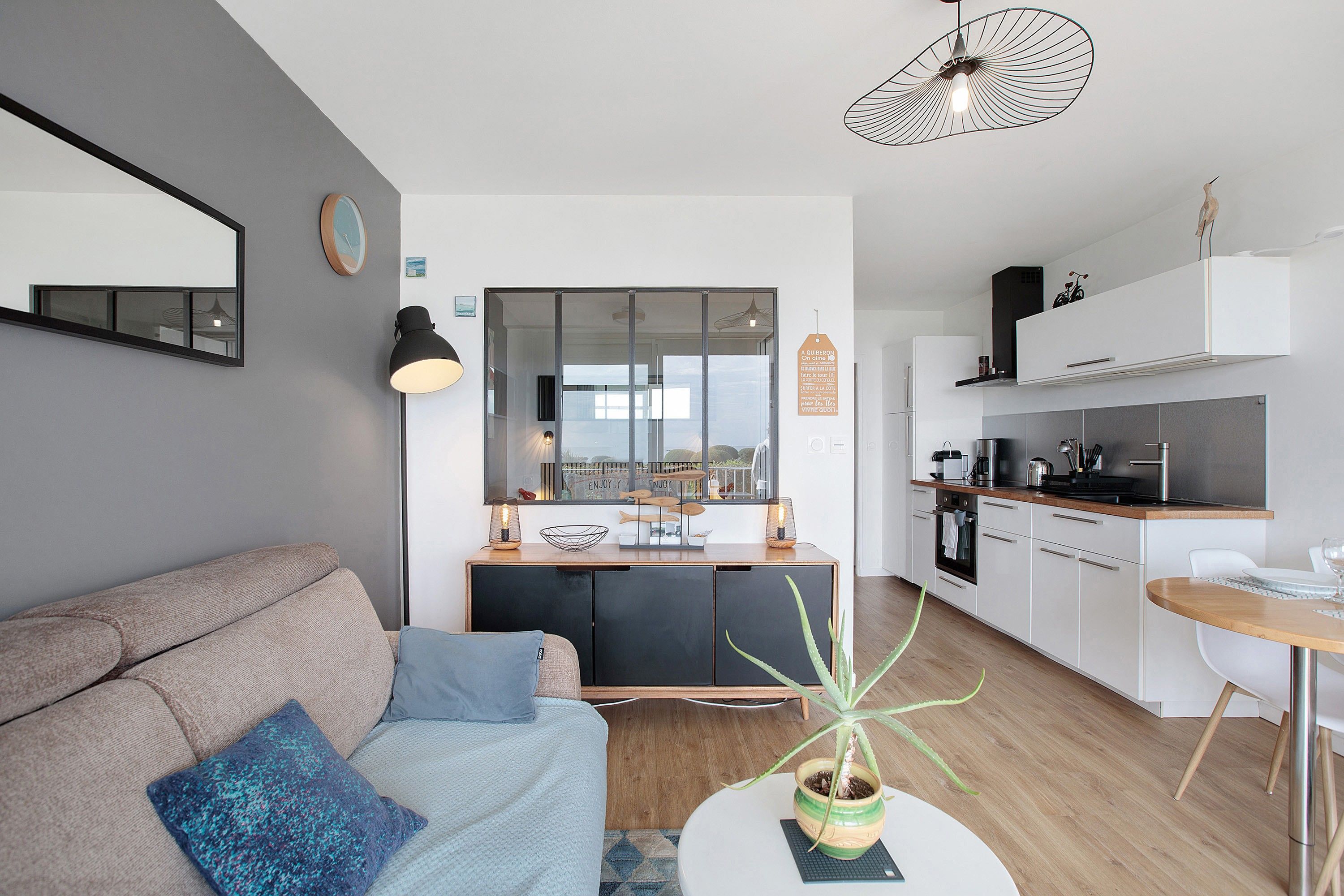 A modern living space with a sofa, a small table with a plant, a dining area, and a kitchen.