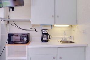 Una kitchenette compacta equipada con microondas, cafetera y lavamanos.
