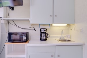 A compact kitchenette with a microwave, coffee maker, and a sink.