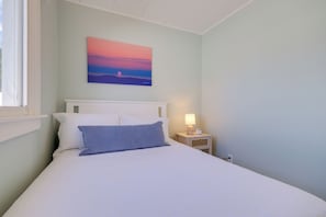 Un dormitorio con una cama, una mesita de noche con lámpara y un cuadro en la pared.