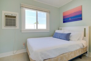 Un dormitorio con cama, ventana con persianas, equipo de aire acondicionado y un cuadro en la pared.