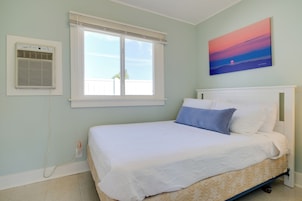 A bedroom with a bed, a window with blinds, an air conditioning unit, and a painting on the wall.