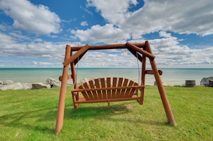 Un conjunto de columpios de madera en un césped con vista al océano y a las rocas.