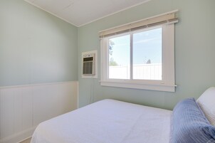 Un dormitorio con una cama individual, una ventana con persianas y un equipo de aire acondicionado instalado en la pared.