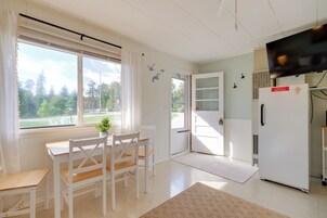 A room with a dining table and chairs, a refrigerator, a door with a window, and a view of trees outside.
