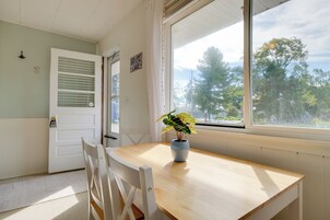 Una habitación con una mesa de madera, una silla blanca, una ventana con vistas a árboles y una puerta con un cartel.