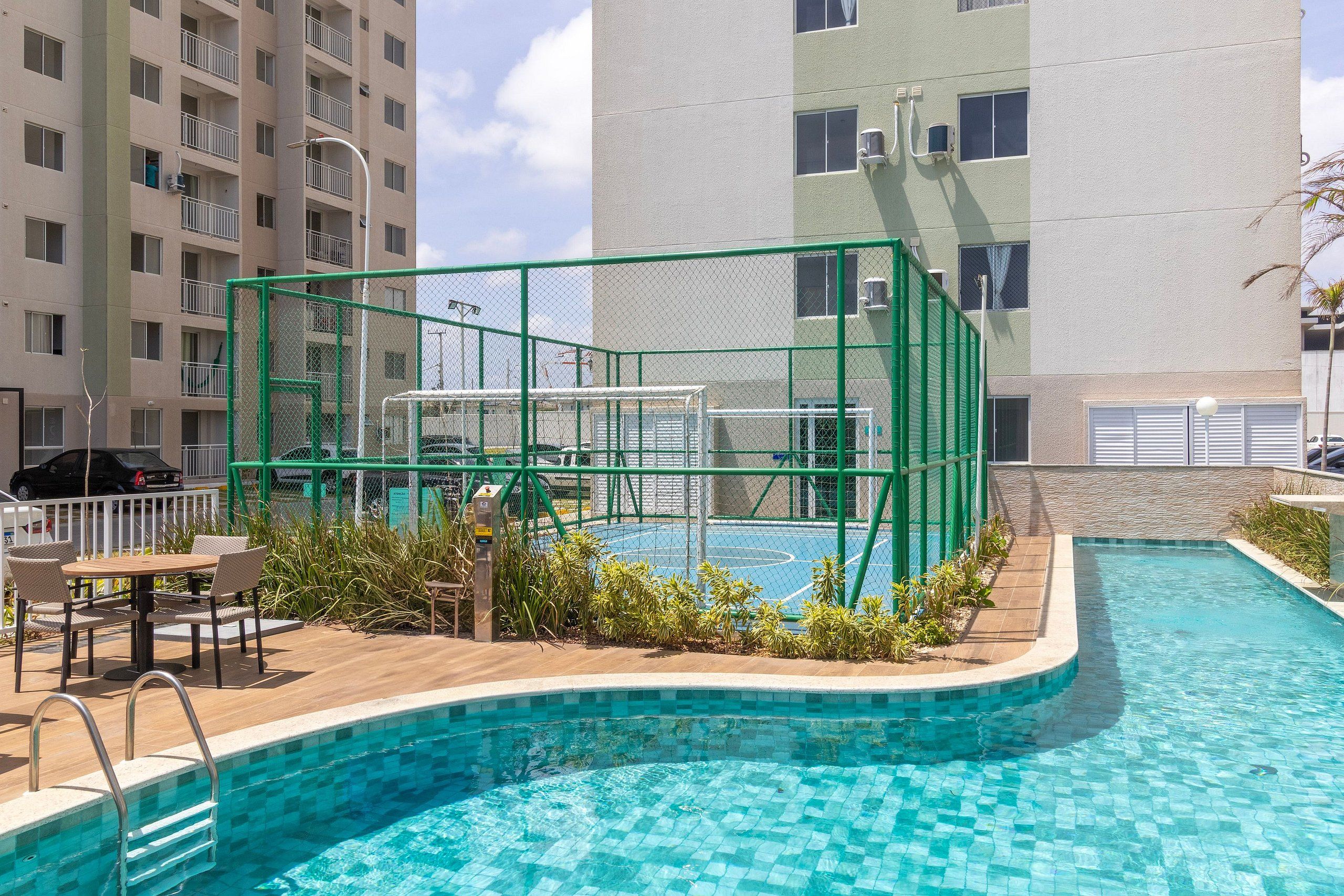Una piscina con una estructura verde de seguridad, rodeada por una terraza de madera y mobiliario de exterior.
