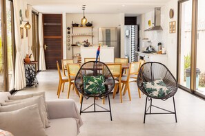 A modern living room with a sofa, dining area with chairs, and a kitchen with appliances.