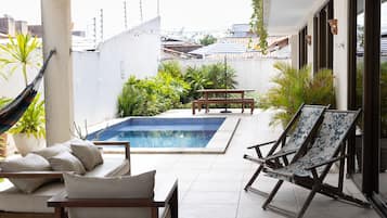 A pool area with a hammock, lounge chairs, and a table.