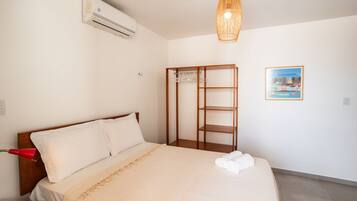 Une chambre d’hôtel avec un lit, une armoire, un appareil de climatisation, un luminaire suspendu et une affiche représentant un paysage urbain accrochée au mur.