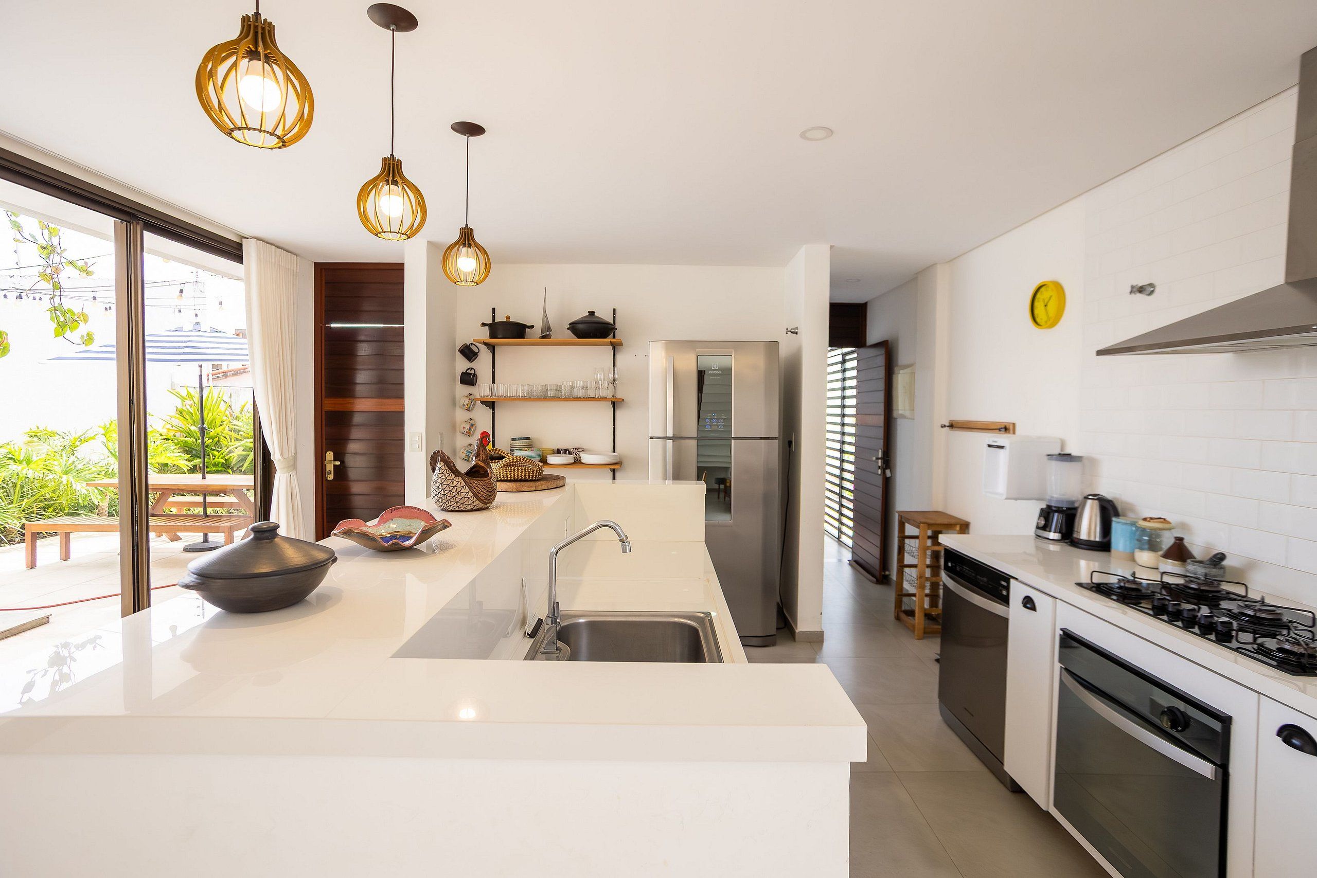 Une cuisine moderne dotée d’un grand îlot central, d’appareils électroménagers en acier inoxydable et de luminaires suspendus.