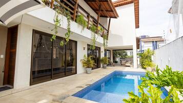 A modern outdoor pool area with a tiled deck, a small pool, and potted plants.