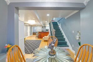 A dining area with a table, chairs, a decorative centerpiece, a staircase, and a kitchen in the background. - Updated Schenectady Home: 1 Mi to Downtown! (Schenectady)