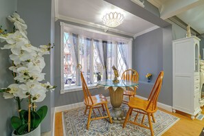A dining area with a glass table, wooden chairs, a chandelier, and a view through sheer curtains. - Updated Schenectady Home: 1 Mi to Downtown! (Schenectady)