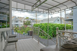 A covered outdoor balcony with a metal railing, a wooden deck, and a view of residential houses in the background.