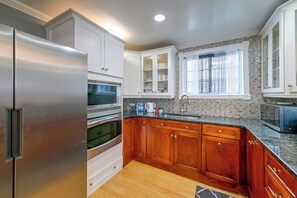 A kitchen with a stainless steel refrigerator, wooden cabinets, a tiled backsplash, and a window with curtains.