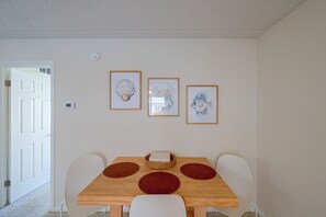A dining area with a wooden table, white chairs, and three framed artworks on the wall. - Walk to Beach! Updated Brigantine Retreat (Brigantine)