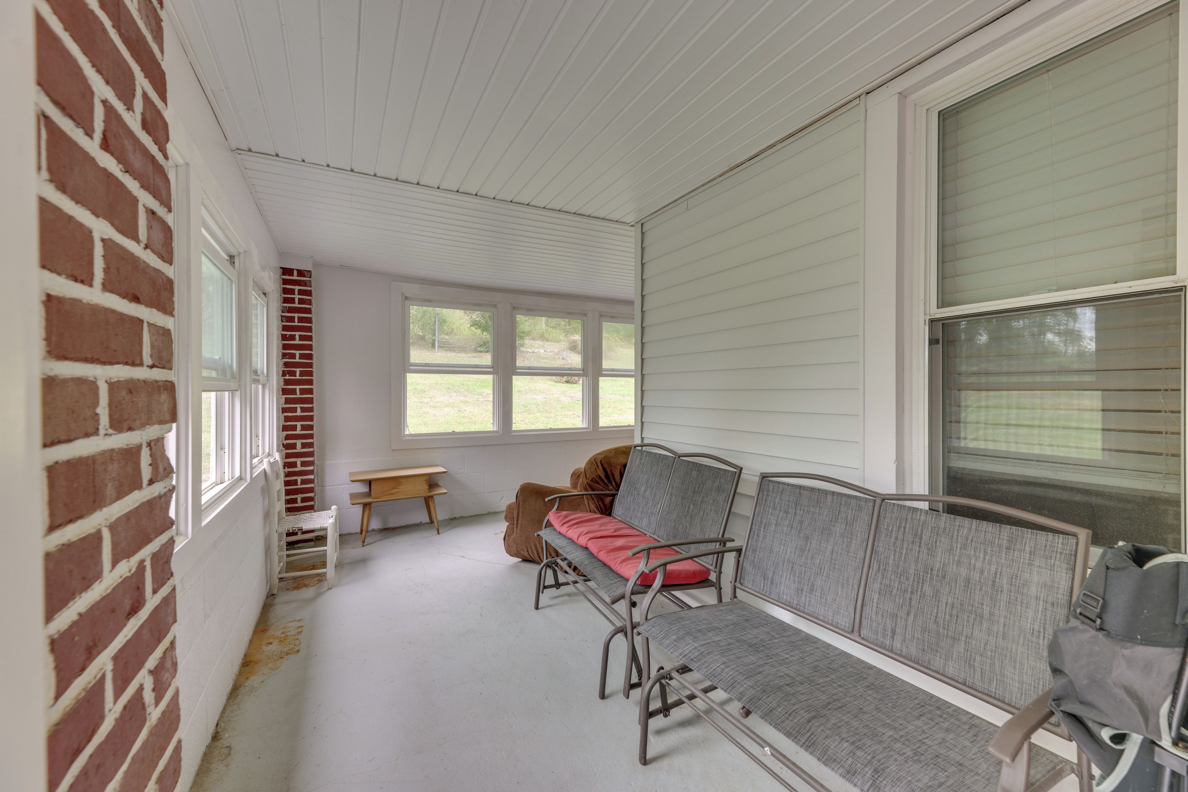 A covered porch with a bench, a table, and a brick wall.