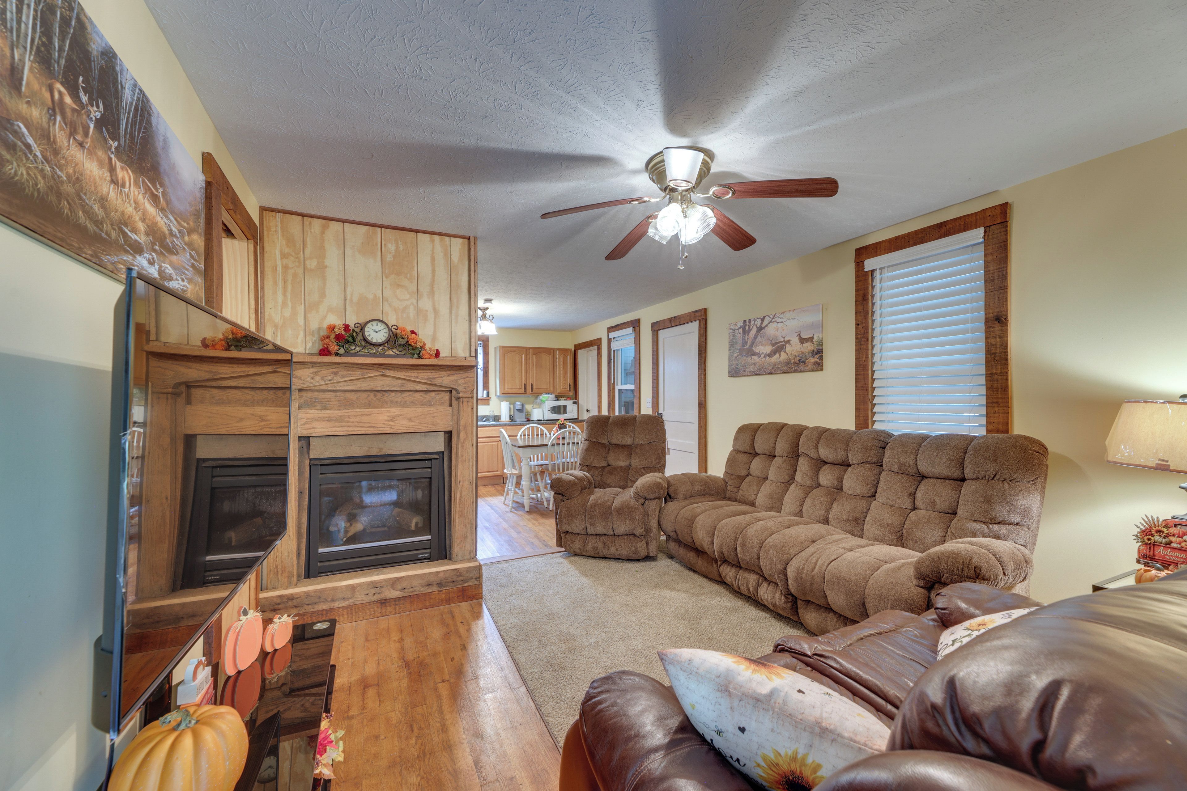 A living room with a fireplace, a ceiling fan, and a dining area in the background.