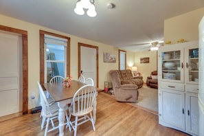 A dining area with a wooden table and white chairs, a living room with a brown sofa and a cabinet with glass doors, and a ceiling fan. - Rural WV Escape w/ Hilltop Mountain Views (Mabie)