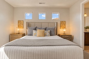 A bedroom with a large bed, two bedside tables, a headboard, and three windows. - Grand Resort #98 9 Bedroom Home (Ivins)
