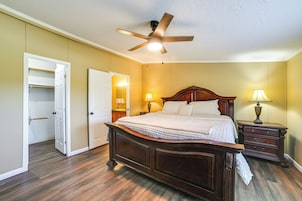 A bedroom with a wooden bed, two bedside tables with lamps, a ceiling fan, and a door leading to a closet.