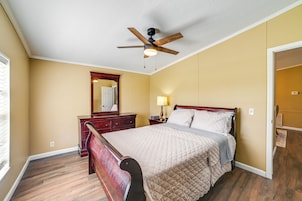 Un dormitorio con una cama de madera, un ventilador de techo, un aparador y un espejo.