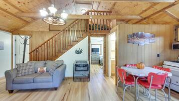 A wooden interior with a sofa, dining table, chairs, a staircase, and a kitchen area.