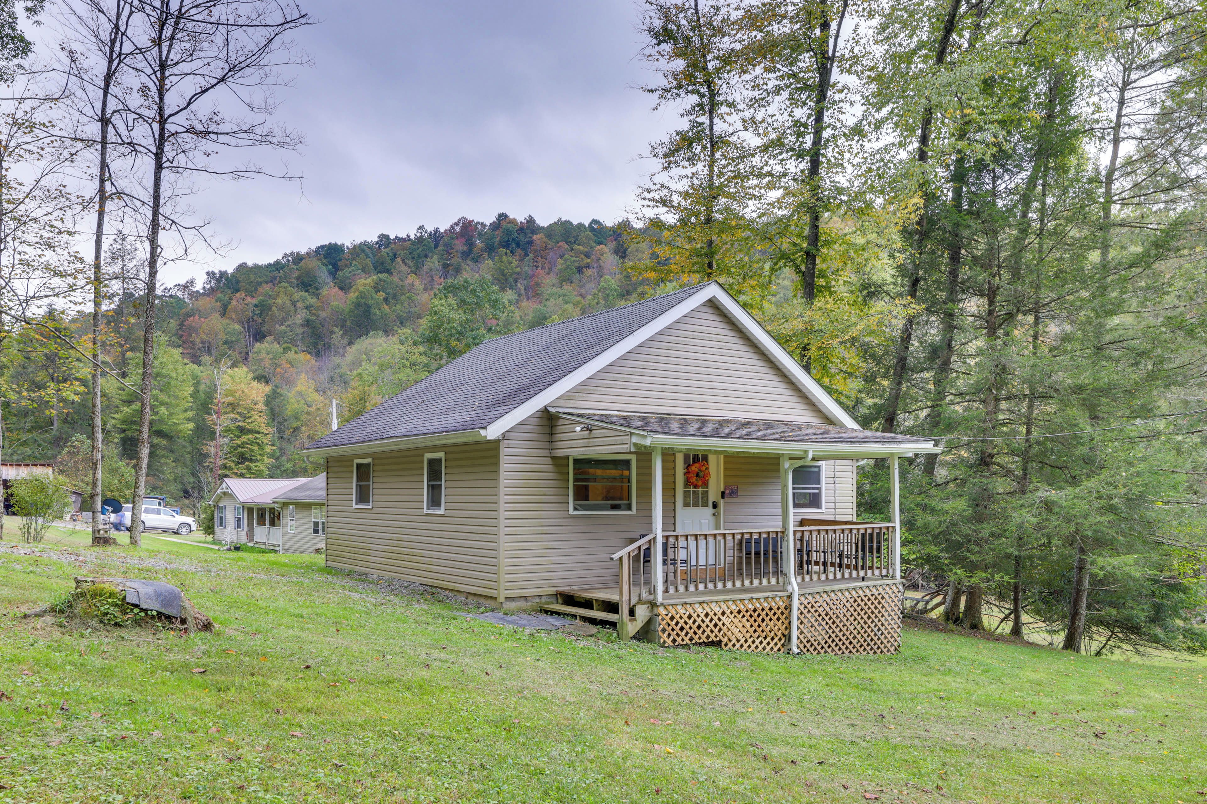 A single-story cabin with a front porch, surrounded by a forested hillside.