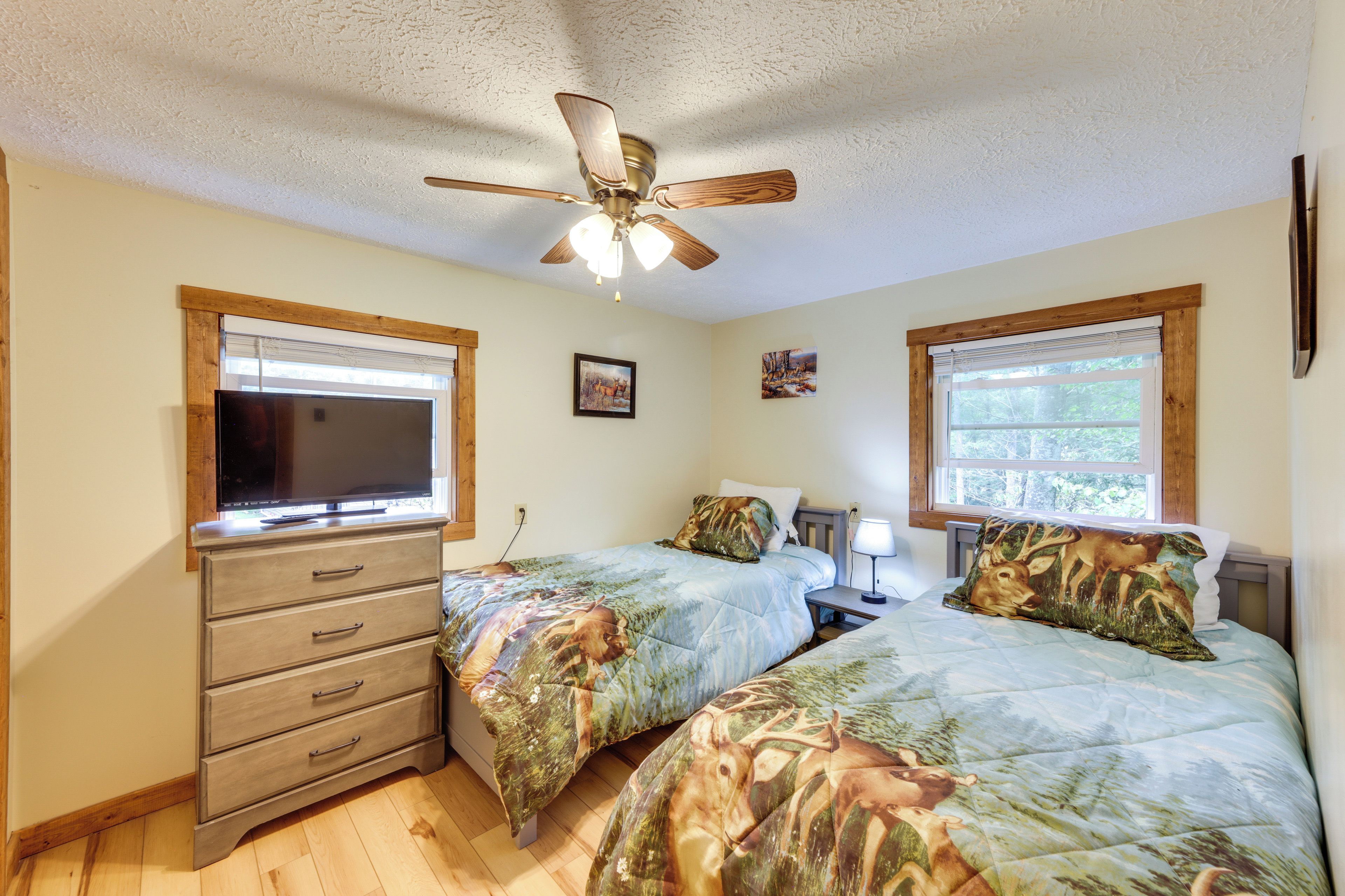 A bedroom with two beds, a ceiling fan, a TV, and a window with blinds.