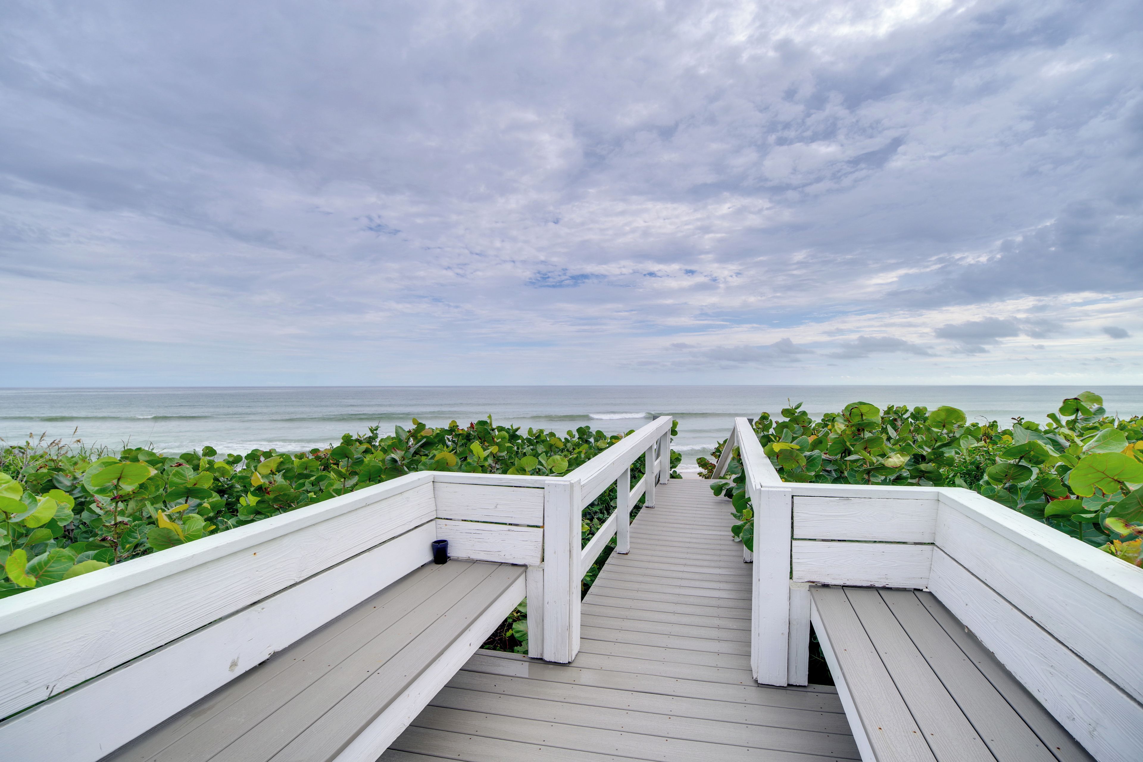 A wooden boardwalk leading to the ocean, surrounded by lush greenery.