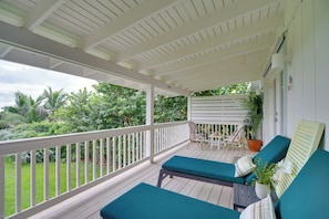 A covered porch with two lounge chairs and a table, surrounded by greenery. - Oceanfront Gem! Steps to Sand, Miles From Ordinary (Vero Beach)