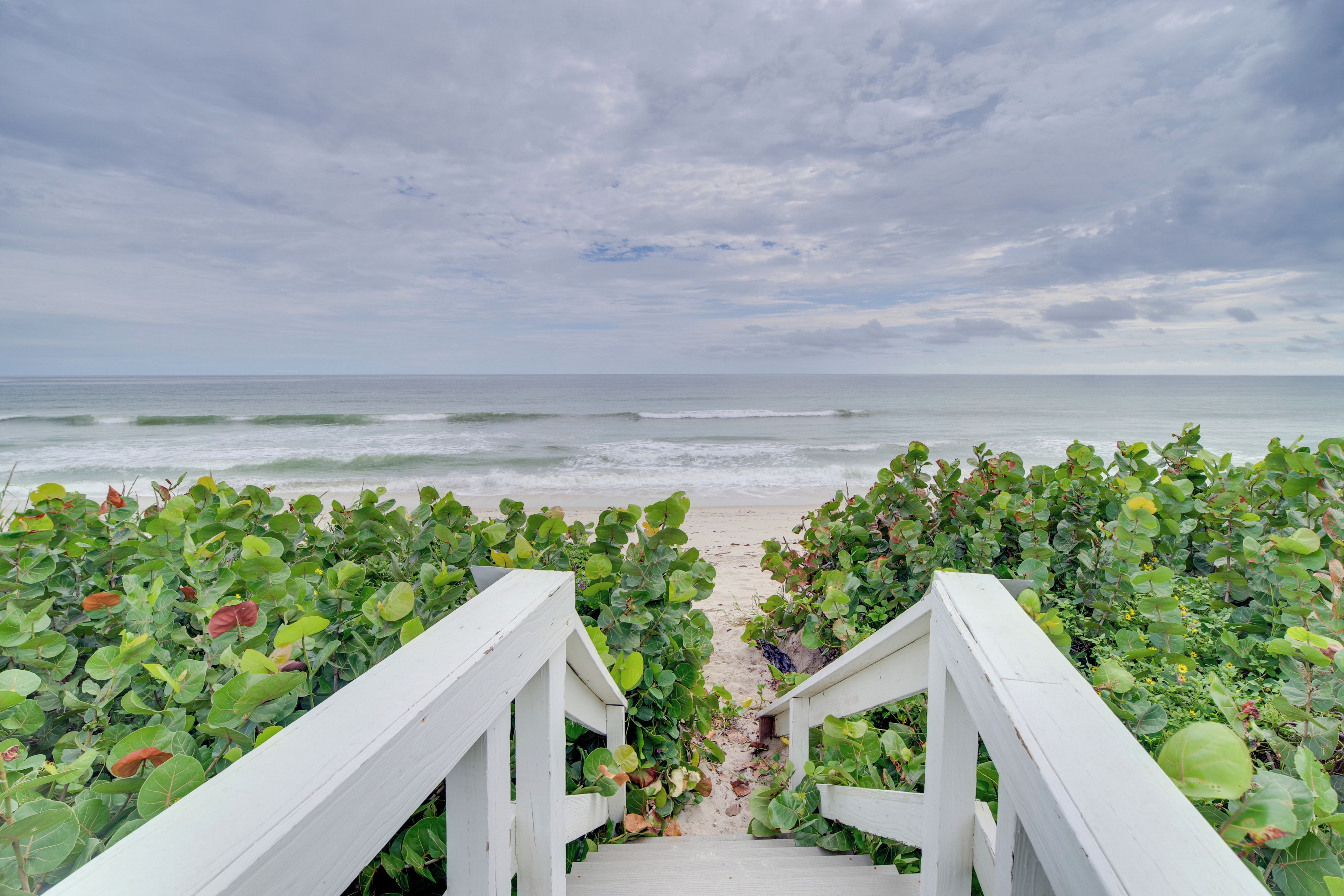 A wooden pathway leading to the beach, surrounded by lush greenery.