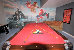 A pool table with a red felt surface, surrounded by a sofa and a wall with superhero-themed artwork. - Luxury 8 Bedroom Villa, Pool/Spa 8 Villa (Kissimmee)
