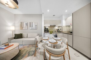A modern living room with a sofa, dining table set for four, and a kitchen in the background. - Stayshort - Cosy 1 Bedroom in MBR City Sleeps 4 With Balcony (Dubai)