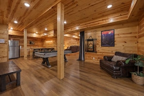 Ein gemütliches Holzinterieur mit Billardtisch, einer Couch, einem Esstisch und einem Kühlschrank.