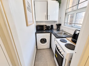 A compact kitchen with a washing machine, a stove, a microwave, and a sink. - 1-bed Apartment in Manchester City Center (Manchester)