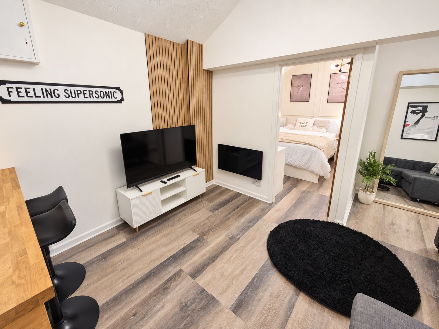 A modern living room with a flat-screen TV, a wooden accent wall, and a black rug.