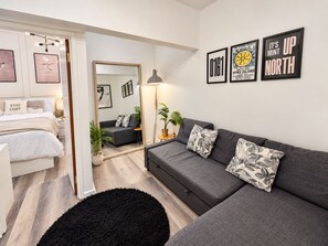 A modern living room with a grey sofa, a black rug, and a bed with a 'STAY COSY' pillow. - 1-bed Apartment in Manchester City Center (Manchester)