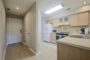 A kitchen with white appliances, wooden cabinets, and a tiled floor. - Beach Days + Hot Tub Nights: Little River Condo (Little River)
