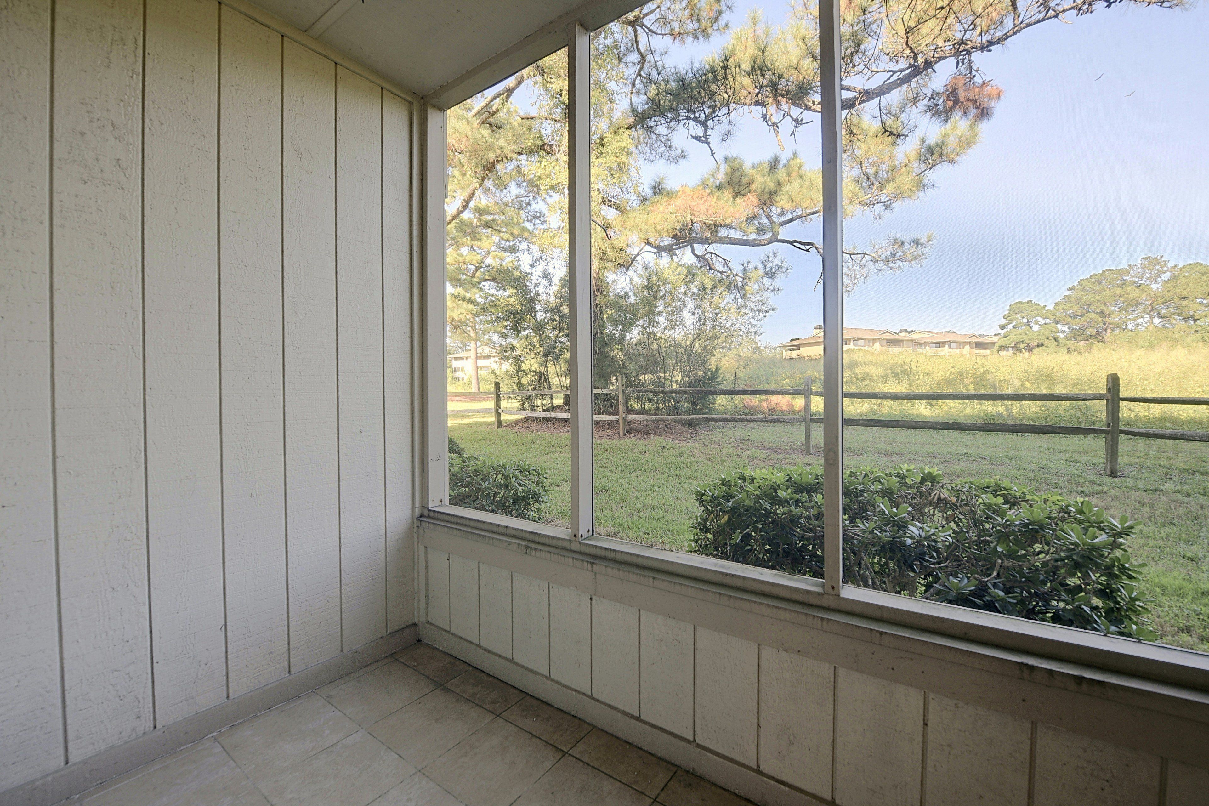 A room with a large window overlooking a grassy area with trees and a fence.