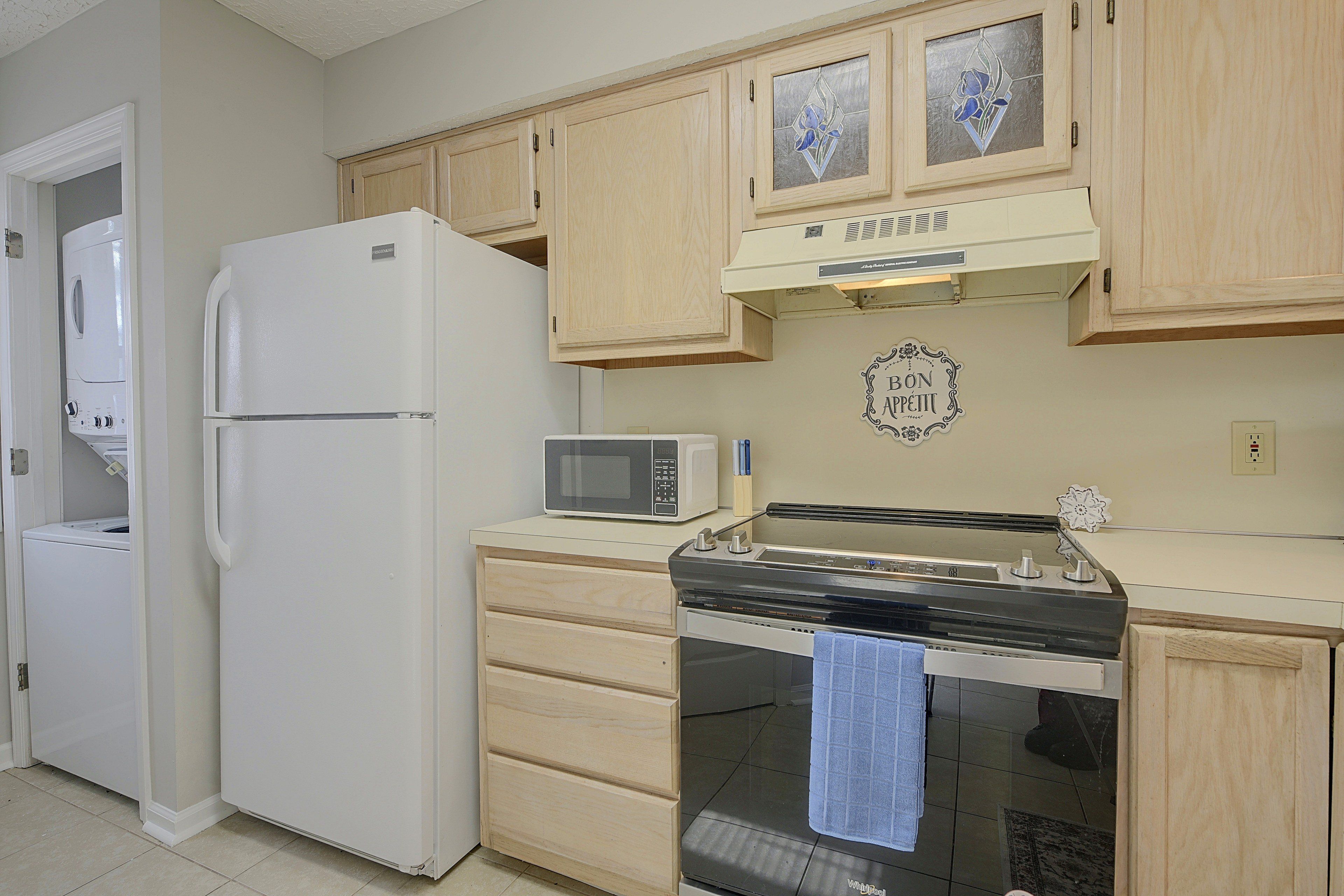 A compact kitchen with a refrigerator, microwave, stove, and wooden cabinets.
