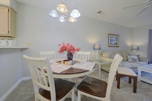 A dining area with a round table, chairs, a vase with flowers, and a ceiling light fixture.