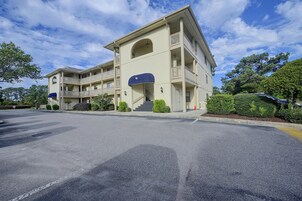 A multi-story hotel with a central entrance, balconies, and a parking lot.